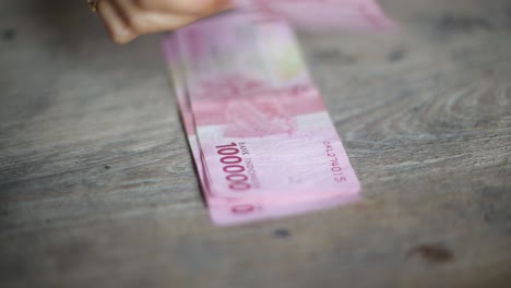 Contando-Dinero-Flujo-De-Caja-De-Rupias-100,000-Notas-Facturas-Indonesia-Con-Fondo-De-Madera