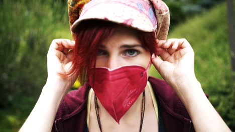 Slow-Motion-Shot-of-red-haired-girl-with-colorful-cap-putting-on-an-red-anti-corona-medical-mask