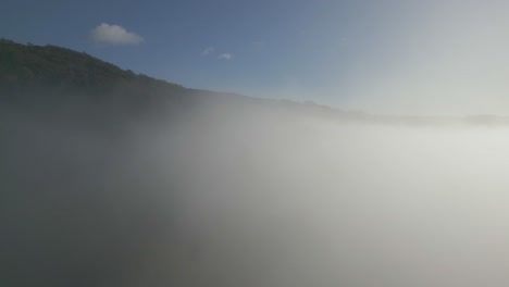 Rising-Drone-Shot-Of-Lake-District-Fells-As-Drone-Rises-Through-Cloud-Inversion-On-Sunny-Autumnal-Morning-With-Blue-Sky-And-White-Clouds