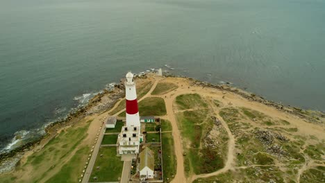 Lighthouse-building-complex-on-sea-coastline,-aerial-orbit-view