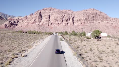 Drone-shot-tracking-a-car-driving-through-Red-Rock-Canyon-in-Nevada,-America