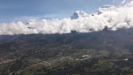 Schwenkdrohnenaufnahme-Des-Schneebedeckten-Huascaran-Gipfels-Mit-Wolken-Neben-Einem-Grünen-Tal-In-Der-Stadt-Yungay-In-Peru