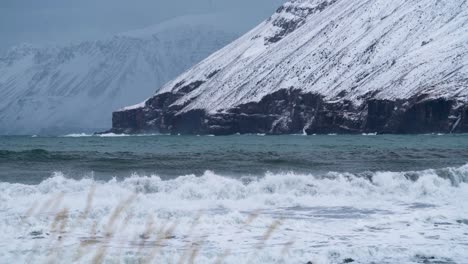 Low-angle-shot-of-Arctic-ocean-waves-hit-the-coast-of-Ólafsfjörður-town-during-cold-freezing-and-snowy-icy-conditions-in-November