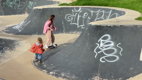 wide-view-of-happy-girl-skateboarding-and-her-brother-running-behind-her-in-summer-in-Estoril,-Cascais