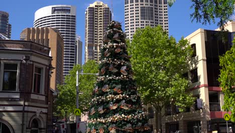 Sydney,-New-South-Wales,-Australien---Weihnachtsbaum-Mit-Wunderschönen-Weihnachtsdekorationen-Und-Hochhäusern-Im-Hintergrund-Bei-Sonnigem-Wetter---Nahaufnahme-In-Zeitlupe