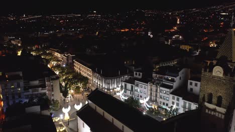 Cathedral-of-Funchal-surrounded-by-Christmas-decorations-on-street-at-night,-aerial