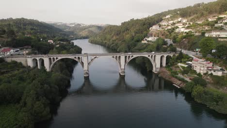 Vista-Aérea-En-órbita-Coches-Cruzando-El-Puente-Entre-os-rios-Sobre-El-Idílico-Río-Tamega