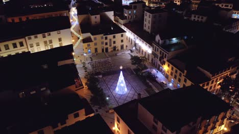 Idyllic-square-with-glowing-Christmas-tree-with-star-in-Madeira-city-at-night,-aerial