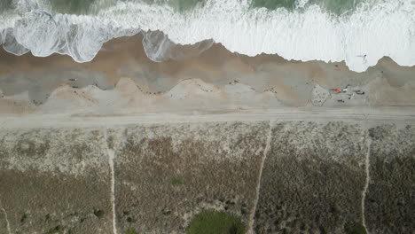 Aerial-top-down-view-tracking-breaking-waves-to-shoreline-Wrightsville-Beach,-North-Carolina