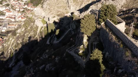 AERIAL---Ancient-city-walls,-Kotor,-Montenegro,-a-UNESCO-World-Heritage-Site,-tilt-down