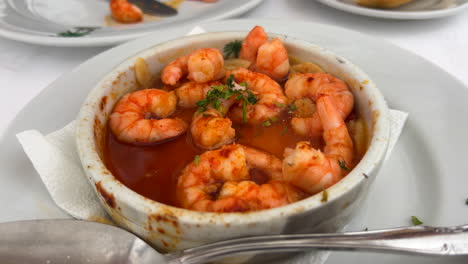 Eating-traditional-Spanish-Gambas-pil-pil-with-bread-in-a-restaurant-in-Marbella-Spain,-delicious-spicy-shrimp-dish-with-garlic,-4K-shot
