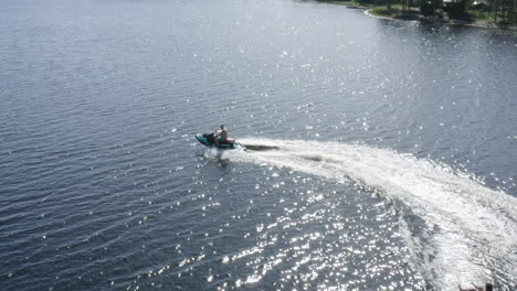 Aerial-view-of-young-men-driving-a-jet-ski-with-a-ringo-ride-in-river-water