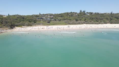 Vista-Aérea-De-Personas-Nadando-Y-Surfeando-En-La-Playa-De-Cilindros-Durante-El-Caluroso-Día-De-Verano---Punto-De-Observación-En-La-Isla-De-North-Stradbroke,-Queensland,-Australia
