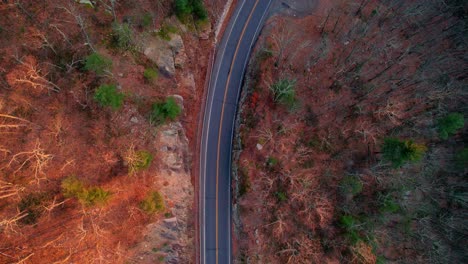 Aerial-drone-top-down-video-footage-of-a-beautiful-mountain-highway-during-fall-autumn-in-the-Appalachian-Mountains,-with-golden-light-at-sunset