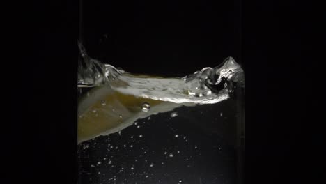 Frische-Zitronenscheibe,-Die-In-Ein-Glas-Wasser-Mit-Schwarzem-Hintergrund-Fällt---Weitschuss,-180-Fps,-Zeitlupe