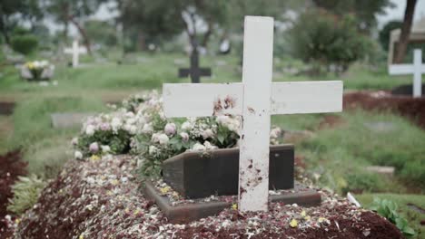 Christian-grave-with-white-cross-and-flower-bouquets-at-cemetery-seen-from-behind