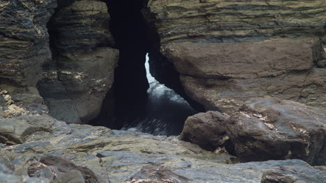 Eine-Lücke-In-Den-Felsen-Mit-Meerwasser,-Das-Durch-Eine-Höhle-In-Portreath,-Cornwall,-Spritzt