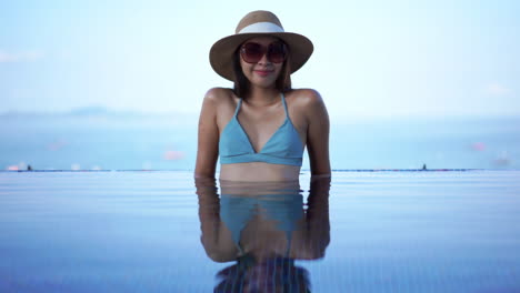 Bella-Mujer-Asiática-En-Bikini-Con-Sombrero-Para-El-Sol-Y-Gafas-De-Sol-Sentada-En-La-Piscina