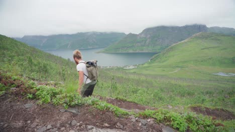 Un-Excursionista-Masculino-Con-Una-Mochila-Subiendo-Cuesta-Arriba-En-El-Pintoresco-Lago-De-Montaña-En-Segla,-Isla-Senja,-Noruega
