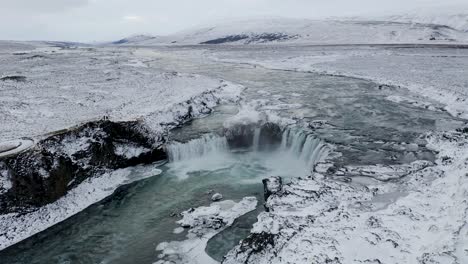 Aerial-approaching-shot-of-beautiful-Godafoss-waterfall-in-North-Iceland-during-snowy-and-iced-winter-day---Tilt-down-shot-of-breathtaking-winter-scene