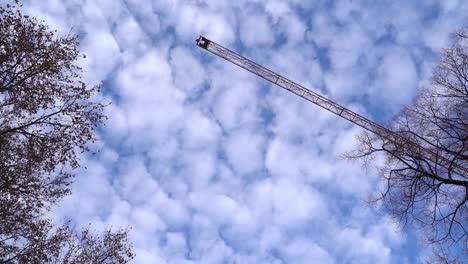 Looking-up-to-construction-crane-slowly-moving-across-blue,-cloudy-sky