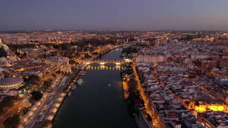 Aerial-view-of-San-Telmo-bridge-at-night-with-Seville-cityscape-panoramic-view