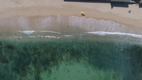 waves-crashing-and-people-passing-in-crystal-water-beach-drone-footage