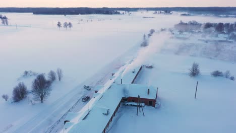 Rural-farm-building-with-smoking-chimney-on-cold-winter-day,-aerial-drone-view