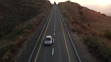 Aerial-view-facing-a-car-driving-down-from-the-highlands-of-Golan-Heights,-sunset-in-Israel---tilt,-drone-shot