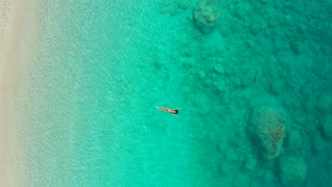 Aerial-view-from-above,-Girl-swimming-on-pristine-water-with-submerged-rocks