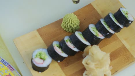 Close-up-for-chef-hands-in-cooking-gloves-squeezing-green-wasabi-sauce-on-a-plate-for-prepared-rolls