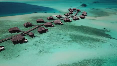 Aerial,-descending,-drone-shot,-towards-a-pier-full-of-bungalows-on-water,-surrounded-by-the-shallow,-turquoise-ocean,-on-a-sunny-day,-on-the-Conrad-Rangali-island,-in-Maldives