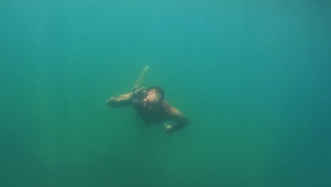 Undersea-scene-of-adult-man-in-apnea-swimming-toward-camera-while-smiling