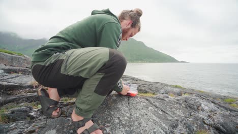 Excursionista-Masculino-Preparando-Su-Caña-De-Pescar-Junto-Al-Lago-De-La-Montaña-Segla-En-La-Isla-Senja,-Noruega