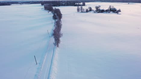 Farmer-transporting-hay-bales-on-icy-winter-road-with-tractor,-aerial-drone-view
