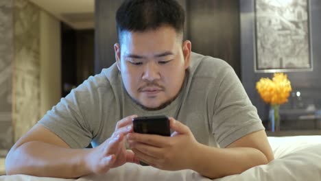 Asiatischer-Mann,-Während-Er-Mit-Dem-Handy-Chattet-Und-Im-Schlafzimmer-Auf-Dem-Bett-Liegt