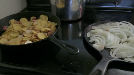 Sliced-potatoes-and-onions-cook-in-two-separate-frying-pans-on-stove-in-home-kitchen-on-induction-stove