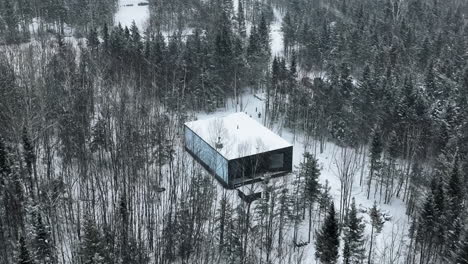 Flying-Above-Mirrored-Cabin-On-Winterly-Forest-In-Charlevoix,-Quebec-Canada