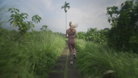 Blond-woman-in-great-physical-shape-jogging-on-Campuhan-ridge-at-sunrise,-Bali
