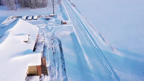 Man-plowing-farm-building-parking-lot-on-cold-winter-day,-aerial-fly-view