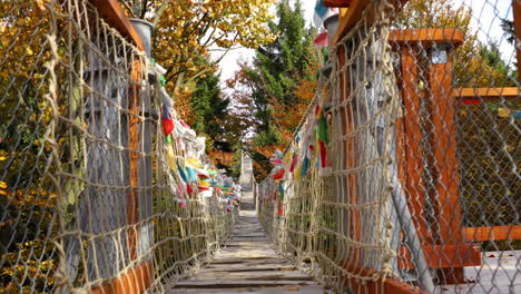 Himalayan-sidewalk,-deep-in-nature-Skywalk-wooden-construction-of-viewpoint-hitting-by-strong-wind-tree-trunks-colored-flags-during-sunny-autumn-day-captured-in-Radhost,-Pustevny-area-4k-60fps