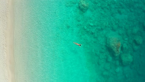 Top-down-descending-beautiful-girl-relaxing-floating-on-Crystal-clear-Seashore,-Greece