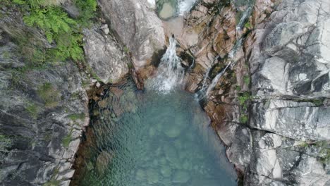 Top-down-slowly-tilt-up-emerald-Natural-pool-through-small-cascade,-Portela-do-Homem---Gerês