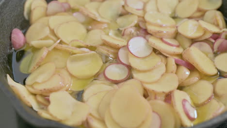 Sliced-potatoes-cook-in-a-lot-of-fat-in-pan,-closeup-static-shot