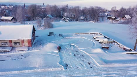 Person-blowing-snow-with-gasoline-equipment-near-farm-building,-drone-flying-close-shot