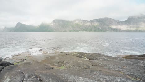 Excursionista-Pescando-En-La-Orilla-Del-Mar-En-El-Parque-Nacional-Anderdalen-En-La-Isla-Senja,-Segla-Noruega-Con-Montañas-Al-Fondo
