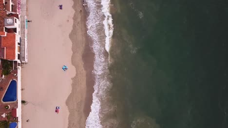 drone-aerial-view-top-down-of-relaxing-view-of-green-ocean-waves-crashing-onto-brown-sandy-Mexican-beach-in-Puerto-Vallarta-at-sunset