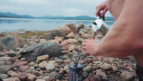 Hiker-Pouring-Coffee-From-Portable-Coffee-Maker-By-the-Lake-Of-Anderdalen-National-Park-In-Senja-Island,-Norway-With-Mountains-In-The-Background