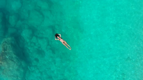 Top-down-approaching-Beautiful-girl-in-bikini-relaxing-on-Emerald-crystal-water,-Greece