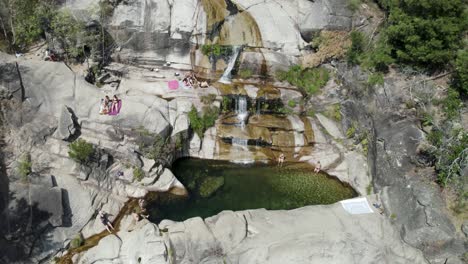 Aerial-view-people-relaxing-on-Tahiti-Cascade-natural-pool-surrounded-by-rocks,-Gerês